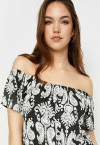 Top negro y blanco sin mangas con un patrón floral, tela texturizada, cierres de botones en el frente y mangas cortas.