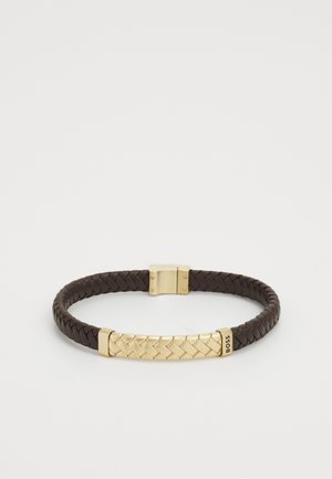 Rudas pintas odinis apyrankė su auksiniu metaliniu užsegimu, turinčiu nertą dizainą ir blizgų paviršių. Prekės ženklas ant vieno metalinio akcento.