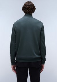 Sudadera verde con cuello alto y mangas largas, que presenta una textura suave y puños y dobladillo acanalados, mostrada desde la parte trasera.