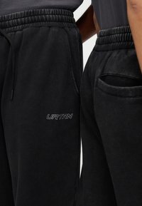 Μαύρο παντελόνι φόρμας με απαλό ύφασμα, διαθέτει ελαστική μέση, κορδόνι, πλαϊνές τσέπες και λευκό λογότυπο "URTRN" στο μηρό.