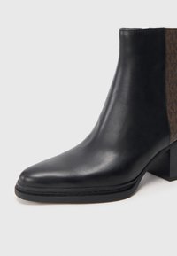Bottine en cuir noir avec talon bloc et panneau latéral élastique marron, finition élégante et lisse, sur fond clair.