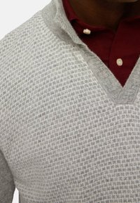 Maglione grigio a maglia con un motivo a scacchi testurizzato, caratterizzato da un design a V che si sovrappone a una camicia color bordeaux con colletto.