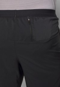 Pantalones cortos deportivos negros con un bolsillo con cremallera, tejido elástico y paneles texturizados en la cintura para mayor comodidad y funcionalidad.