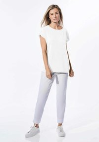 Top bianco a maniche corte con una vestibilità comoda, abbinato a pantaloni grigi chiari a vita alta e sneakers bianche. Tessuto liscio e design semplice.