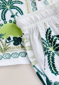Medvilniniai šortai su žaliu botaniniu raštu, elastiniu liemeniu ir balta baze. Išskirtiniame dizaine – sudėtingi lapų raštai.