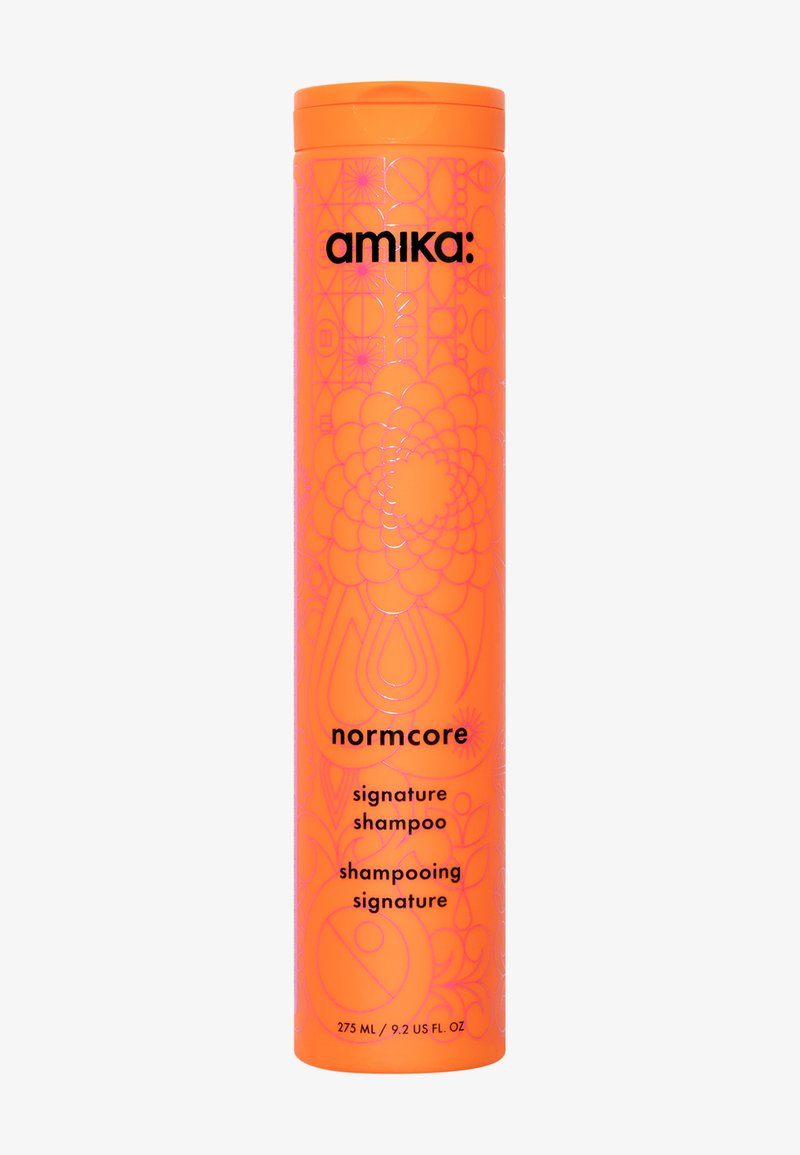 Flacon cylindrique orange de shampooing Amika Normcore Signature. Présente des motifs géométriques, un texte noir et un bouchon blanc. Contenance de 275 mL.
