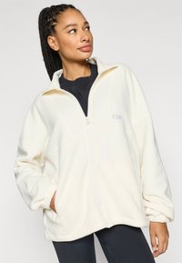 Off-white-värinen fleecetakki, jossa on korkea kaulus, edessä vetoketju, sivutaskut ja joustavat hihansuut. Sisältää hillityn logopistelyn.