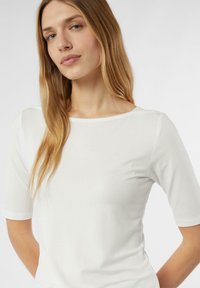 Biała koszulka z krótkim rękawem z okrągłym dekoltem, gładką fakturą i dopasowanym krojem. Tkanina wydaje się miękka i lekka.