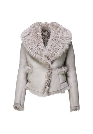 Femme portant une veste gris clair bordée de fourrure, un pantalon court gris foncé, des chaussures beiges à petit talon, et tenant un petit sac à main noir.