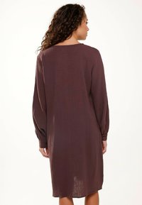 Abito a maniche lunghe, dalla vestibilità ampia, in un profondo bordeaux, caratterizzato da un tessuto testurizzato e una silhouette rilassata, che arriva fino a metà coscia.