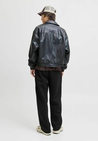 Schwarze Kunstlederjacke mit elastischem Saum, kombiniert mit lockeren schwarzen Hosen und einer zweifarbigen Mütze. Glatte Textur und lässige Passform.