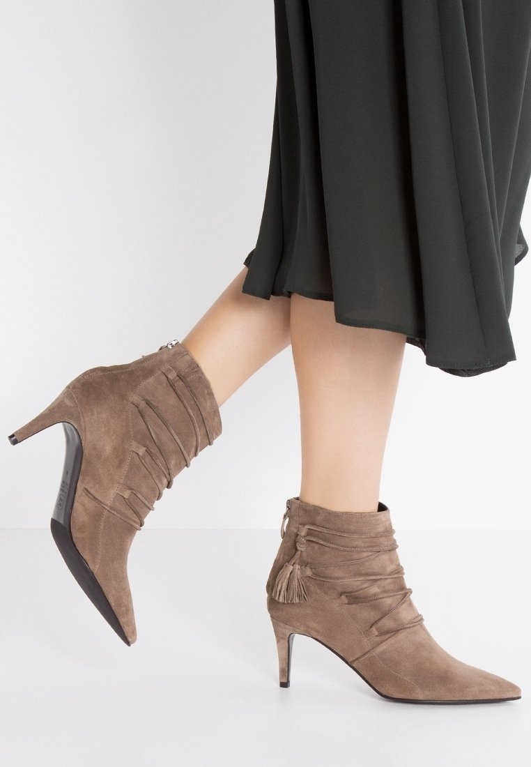Botas de tobillo de suede topo con punta afilada, diseño arrugado, textura agrupada y acentos decorativos de borlas. Tacón de aguja.