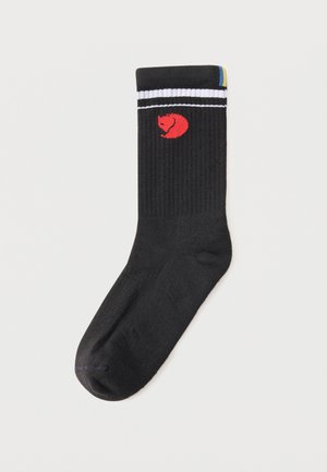 Sort crew-sok med en rød krøllet rævelogo nær toppen, hvide dobbelte striber under kanten og en lille blå og gul detalje på kanten.