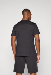 Svart t-skjorte med korte ermer og jevn tekstur, med en kontrastfarget meshpanel bak, kombinert med svarte shorts med sidelommer.