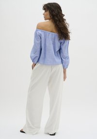 Blauwe en witte gestreepte off-the-shoulder blouse met elastische halslijn en lange pofmouwen, gecombineerd met vloeiende witte wijdere broeken.