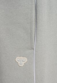 Pantalons de survêtement en tricot gris clair avec un tissu texturé, une bande d'accent blanche et un petit emblème brodé avec des motifs floraux.