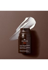 Brun cylindrisk behållare med en svart pump topp. Vit gel pressas ut vid sidan av. Etiketten har vit och orange text.