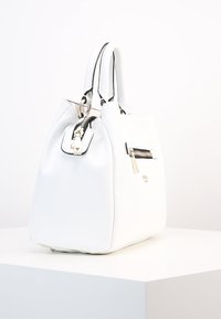 Biała skórzana torba o sztywnej formie, z zaokrąglonymi uchwytami, srebrnymi okuciami oraz małą kieszonką na zamek po boku.