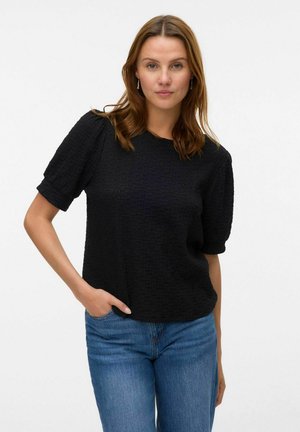 Haut noir texturé à manches courtes avec un col rond et une coupe décontractée. Associé à un jean en denim bleu. Design simple avec un motif en relief.