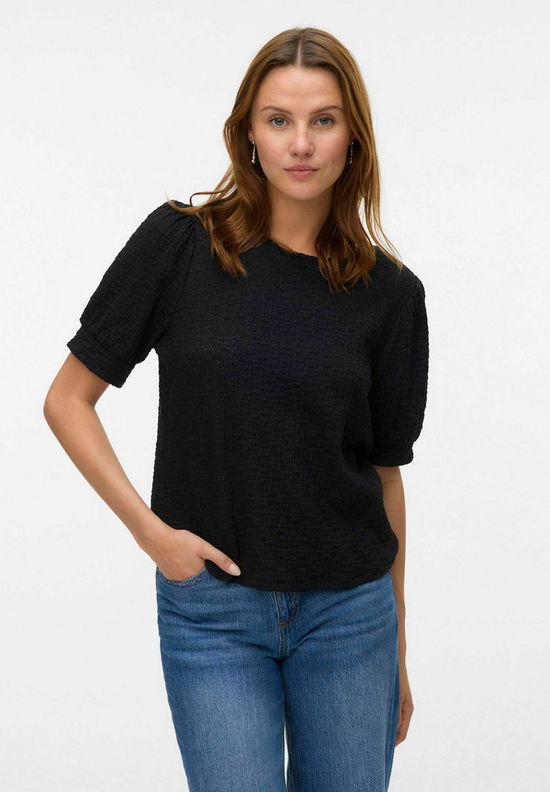 Zwart gestructureerd T-shirt met korte mouwen, ronde hals en een losse pasvorm. Gecombineerd met blauwe denim jeans. Eenvoudig ontwerp met een verhoogd patroon.