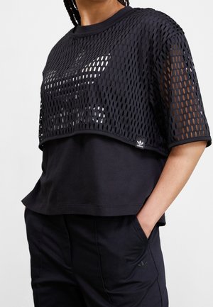Schwarzes Kurzarmoberteil mit Netzüberzug und einer inneren Schicht darunter. Verfügt über ein Logopatch am Saum und eine lockere Passform.