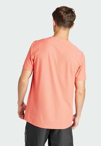 Camiseta de manga corta en color coral, hecha de tejido transpirable. Presenta un cuello redondo y un corte holgado, con una textura suave y detalles de costura sutiles.