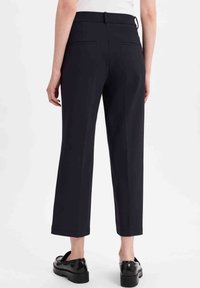 Marineblauwe high-waisted broek met een recht model, voorzien van twee achterzakken en een subtiele textuur. Gepaard met zwarte platform schoenen.