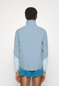 Veste bleu clair avec un motif texturé, col montant et accents bleu clair contrastants sur les manches. Offre une coupe moderne et décontractée.
