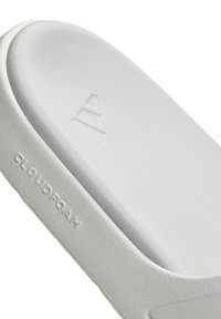 Chancla blanca Cloudfoam con suela texturizada, superficie superior lisa y logotipos en relieve. Material duradero y diseño minimalista.