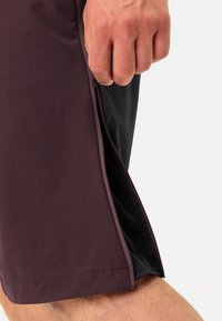 I pantaloni corti in tessuto bordeaux scuro presentano una zip laterale e una fodera in rete, con un orlo dritto e una texture liscia.