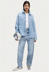 Světle modrá džínová bunda s volným střihem, předními kapsami a stříbrnými knoflíky, doplněná o volné džíny stejné barvy a lesklé stříbrné baleríny.