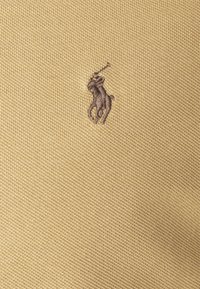 Žluté polo tričko s texturovanou látkou a malým hnědým vyšitým logem jezdce na levé části hrudi.