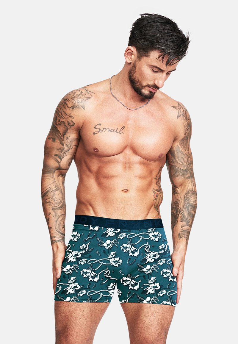 Herrens kalsonger i teal-färgad tyg med blommönster och band. Har ett fast mörkt midjeband. Materialet verkar smidigt och elastiskt.