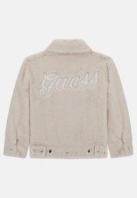 Giacca in pelliccia sintetica beige con colletto, maniche lunghe e un grande logo ricamato "Guess" sulla parte posteriore. Chiusura con bottoni neri.
