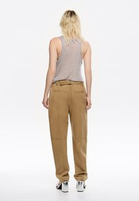 Pantaloni beige a gamba larga con cintura, caratterizzati da dettagli delle cuciture visibili, abbinati a un top grigio a coste e sandali con tacco squadrato argentati.