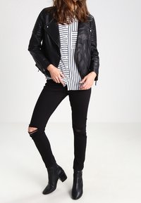 Černá kožená motorkářská bunda s prošívanými detaily, zkombinovaná s bílou a černou pruhovanou blůzou, ošuntělými černými džíny a kotníkovými botami.
