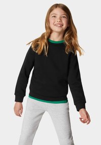 Felpa nera con colletto verde a contrasto, scollatura rotonda e polsini a coste, abbinata a pantaloni della tuta grigio chiaro. Tessuto morbido, vestibilità casual.