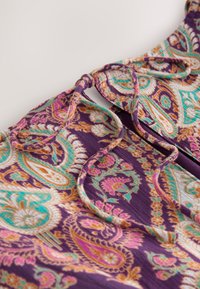 Lilla mustriga kangas, millel on peenikesed paisley-mustrid türkiissinise, roosa ja kullaga. Omab lipsuga kaelust ja pehmet, tekstuurset materjali.
