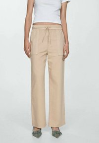 Beige, wijde broek met een trekkoord in de taille, voorzien van twee zijzakken en een gladde textuur, gecombineerd met decoratieve schoenen.