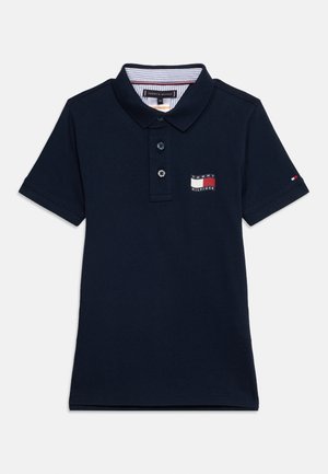 Tumesinist värvi lühikeste varrukatega polo särk, millel on kaks nööpi, allapoole voltuv krae ja Tommy Hilfigeri logo plaastrid rinnal ja varrukal.