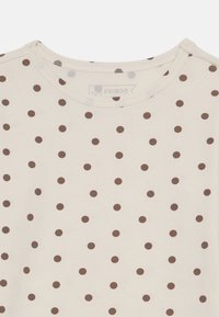 Ljus krämfärgad t-shirt med rund halsringning, prydd med ett upprepande mönster av små bruna prickar på framsidan och en mjuk bomullstextur.