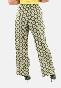 Pantaloni larghi a righe verdi con forme di diamante bianche, vita elastica e taglio svasato, abbinati a tacchi neri.