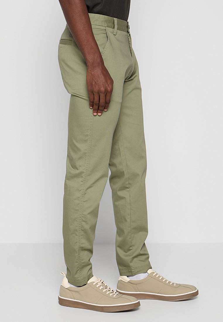Khaki groene chinos met een rechte snit, gemaakt van een katoenmix, met zijzakken en een gladde, gestructureerde afwerking. Draagt met beige sneakers.