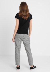 Černý tričko s krátkým rukávem v kombinaci se šedými kostkovanými kalhotami. Oblečení má slim fit a jemné materiály, doplněné černými teniskami.