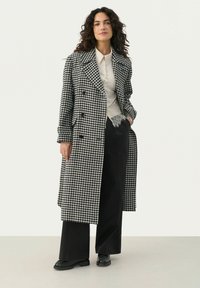 Black and white houndstooth-patterned long coat with double-breasted design, paired with a light top and wide-leg black pants.