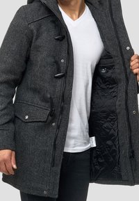 Grau strukturierter Mantel mit Kapuze, ausgestattet mit schwarzen Toggle-Knöpfen, seitlichen Taschen und einem gesteppten schwarzen Innenfutter. Sichtbarer Reißverschluss.