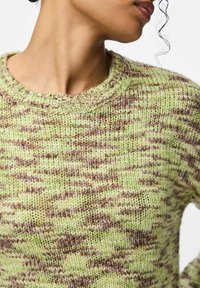Strickpullover mit einem gemischten Muster aus Grün und Braun, geripptem Rundhalsausschnitt und strukturierter Stoffqualität. Sichtbare Nähdetails betonen das Design.