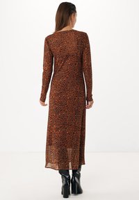 Braunes Kleid mit Leopardenmuster, langärmlig, figurbetont, transparente Textur, bodenlang, kombiniert mit schwarzen Stiefeletten mit Absätzen.