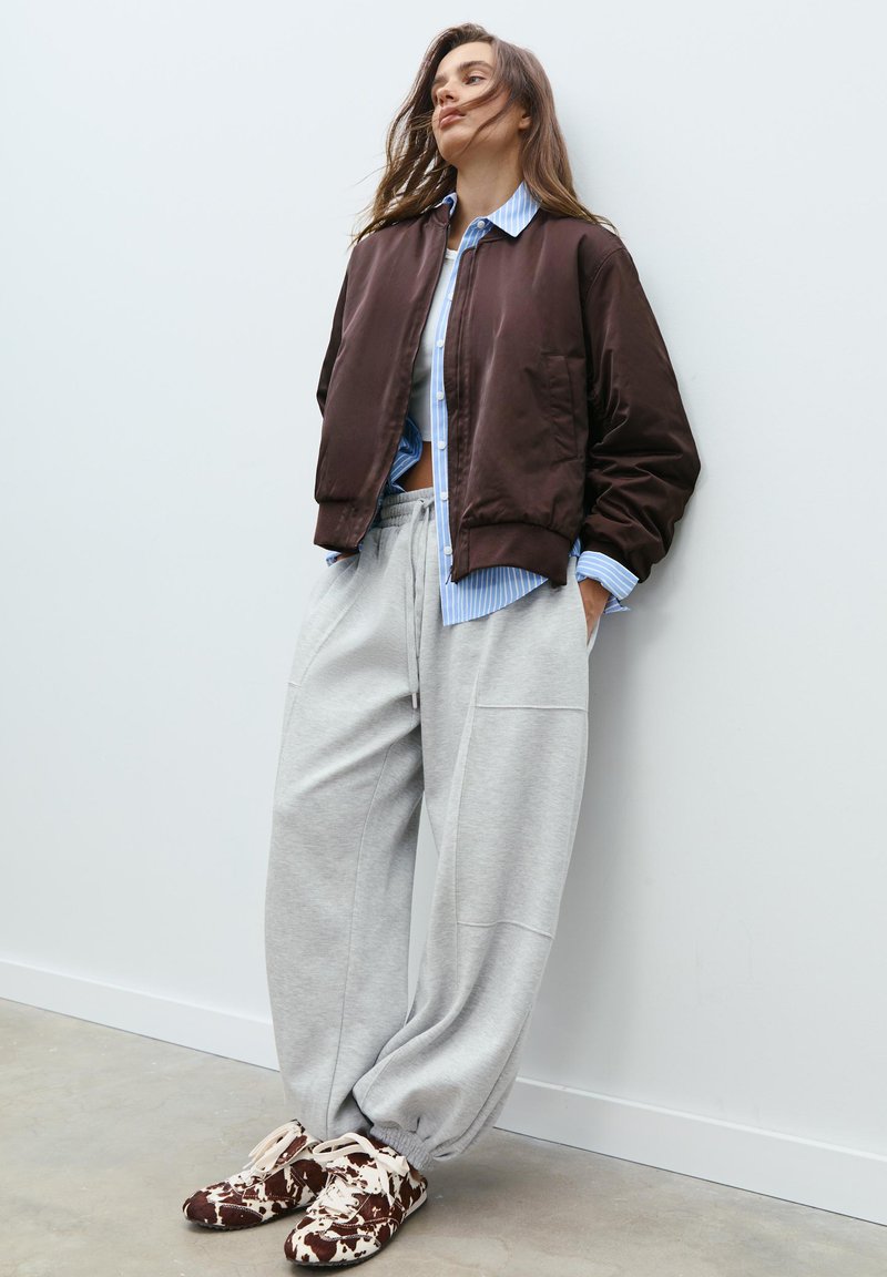 Brown bomber jacket, light blue striped shirt, gray wide-leg sweatpants, and patterned brown sneakers. Smooth textures and relaxed fit.