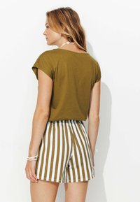 Haut à manches courtes vert olive associé à un short à rayures blanches et brunes. L'ensemble présente une coupe décontractée et des détails de coutures visibles.